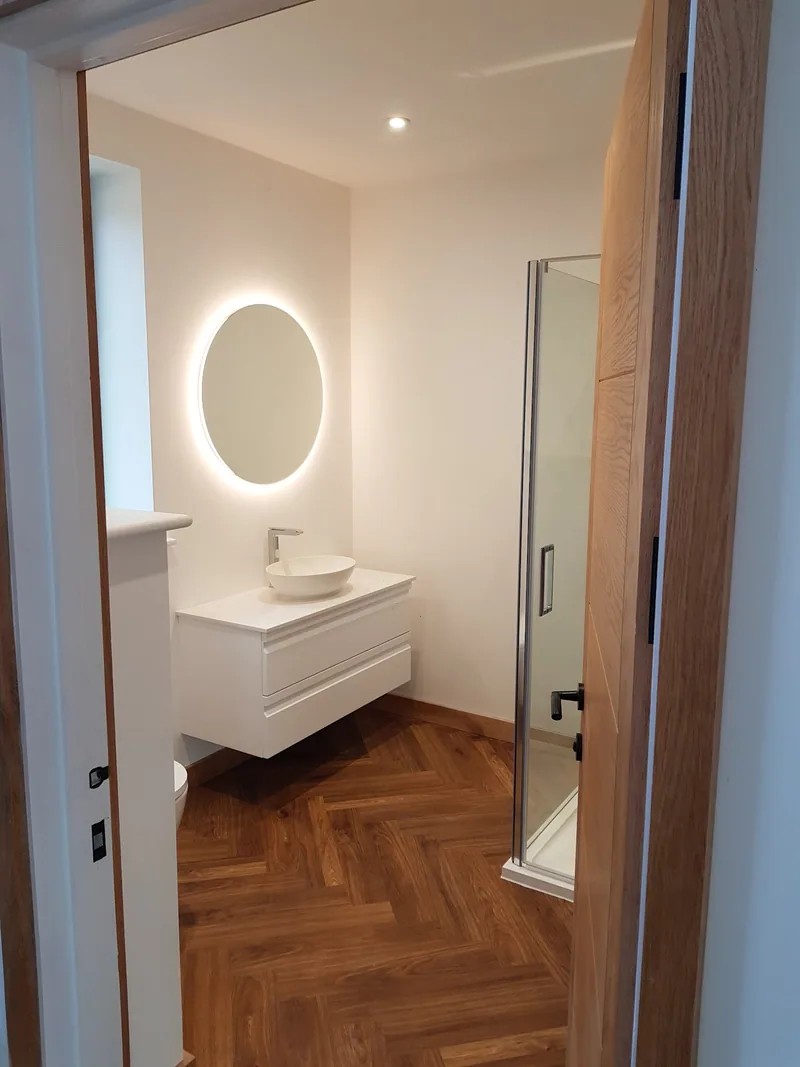 Finished bathroom with a round backlit mirror and ceiling spotlights